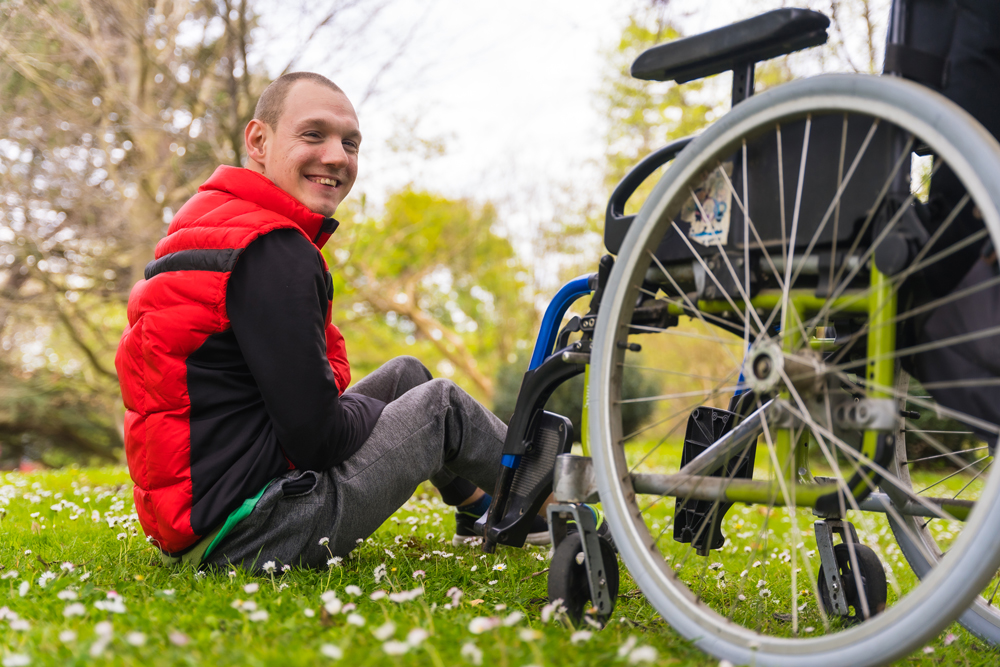 Young man sitting on the grass beside a wheelchair