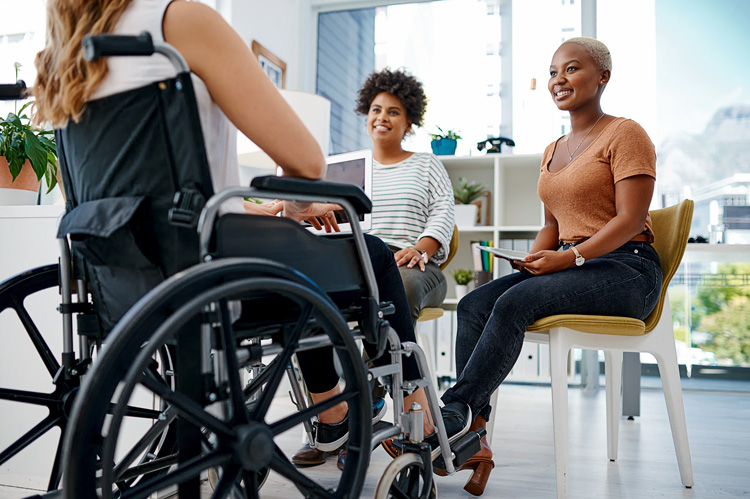 a woman siting in a wheelchair with two other women listening and smiling